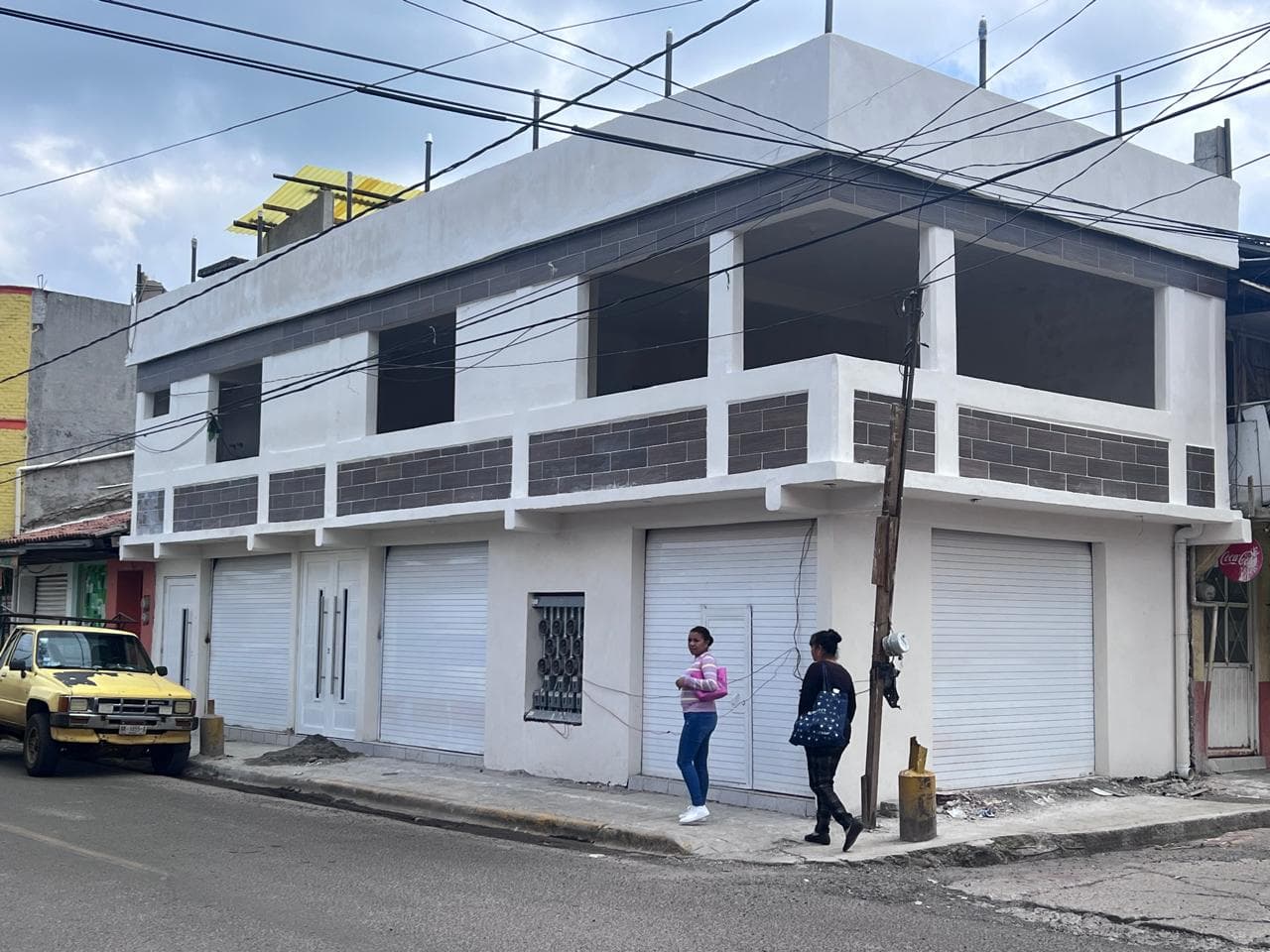 Vista en perspectiva de un inmueble de dos niveles construido con locales comerciales en planta baja y espacios residenciales en la planta superior.